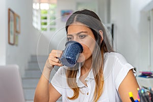 Young latina woman drinking coffee working on a laptop and sitting at homeoffice