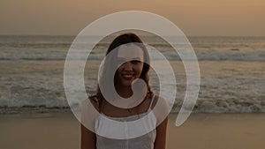 Young latino girl happily having fun and laughing at the ocean. Long dark hair. White dress.