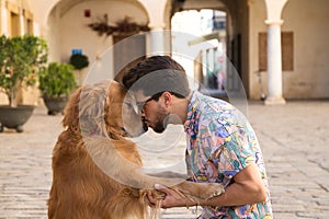 young latino man and his brown golden retriever dog walking in the street. The man kisses the dog on the head with affection.