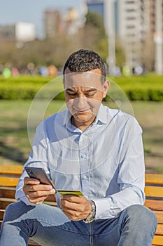 Young Latino man making a purchase with a credit card on his mobile phone in a public park