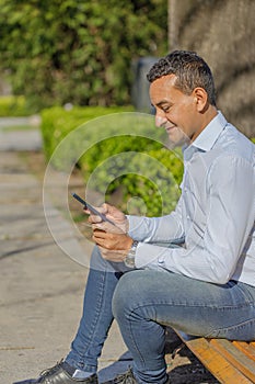 Young Latino man making a purchase with a credit card on his mobile phone sitting on a bench