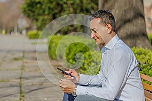 Young Latino man making a purchase with a credit card on his mobile phone sitting on a bench in a public park