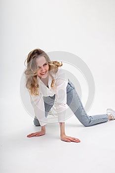 Young laughing caucasian girl in shirt, jeans, standing on her knees on floor