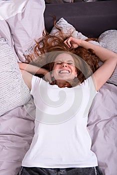 Young laughing woman lying on her bed at home