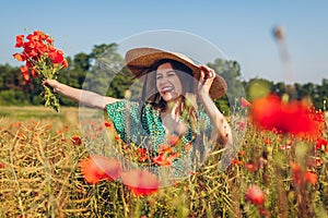 Young laughing woman raised arm holding bouquet of poppies flowers walking in summer field. Happy girl feeling free