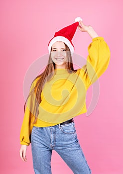 Young laughing woman in santa hat and yellow sweater on pink background