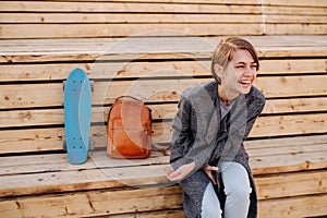 Young laughing woman with a skateboard is sitting on a 2-stage bench.