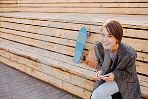 Young laughing woman with a skateboard is sitting on a 2-stage bench.