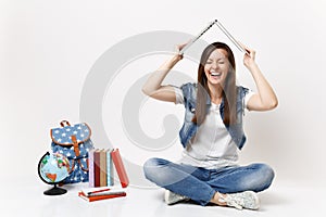 Young laughing woman student with closed eyes holding laptop pc computer above head like roof near globe backpack school