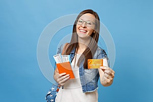 Young laughing woman student in glasses with backpack holding passport boarding pass tickets credit card isolated on