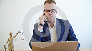 Young lawyer talking mobile phone and working on laptop at table in law office