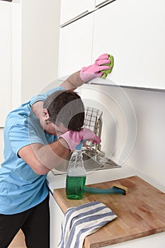 Young lazy house cleaner man washing and cleaning the kitchen with detergent spray bottle