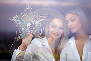 Young lesbian couple holding Christmas star decoration in window