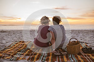 Young lesbian couple watching a romantic sunset at the beach