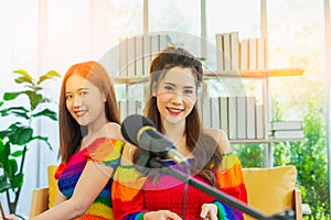 young lgbt couple women happy singing together behind microphone in living room at home