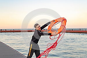 A young lifeguard on the shore throws an orange lifebuoy into the sea