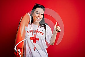Young lifeguard woman wearing secury guard equipent holding rescue float over red background happy with big smile doing ok sign,