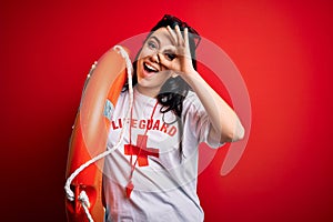 Young lifeguard woman wearing secury guard equipent holding rescue float over red background with happy face smiling doing ok sign