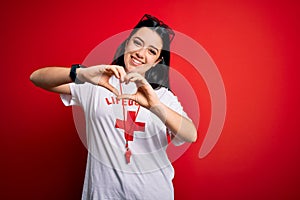Young lifeguard woman wearing secury guard equipent over red background smiling in love doing heart symbol shape with hands