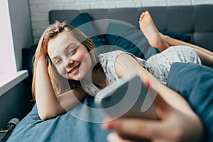 Young light brown hair woman in bed at home. Happy  girl smiling having  video call  on mobile telephone.  Teenager lying in bed a