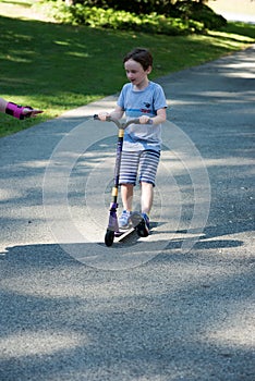 Young litte boy outside riding his scooter in the driveway