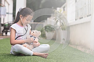 Young little asian girl playing pretend to be a doctor. young girl eaxamine her teddy bear with stethoscope