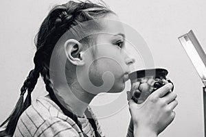 Young little baby girl drinking milk mug coffee tea hot drink. 9 years old girl drinks milk or tea from a cup