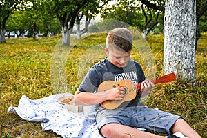 Young little boy guitarist outdoor. Boy on city park summer meadow enjoying day playing guitar.