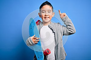 Young little boy kid skateboarder holding modern skateboard over blue isolated background surprised with an idea or question
