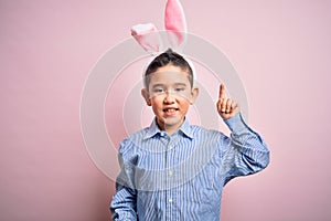 Young little boy kid wearing easter bunny ears over isolated pink background pointing finger up with successful idea