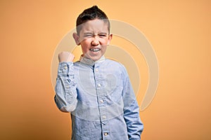 Young little boy kid wearing elegant shirt standing over yellow isolated background angry and mad raising fist frustrated and