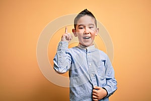 Young little boy kid wearing elegant shirt standing over yellow isolated background pointing finger up with successful idea