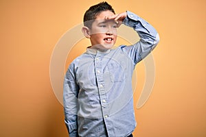 Young little boy kid wearing elegant shirt standing over yellow isolated background very happy and smiling looking far away with