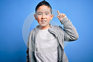 Young little boy kid wearing sport sweatshirt over blue isolated background pointing finger up with successful idea