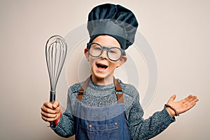 Young little caucasian cook kid wearing chef uniform and hat using manual whisk very happy and excited, winner expression