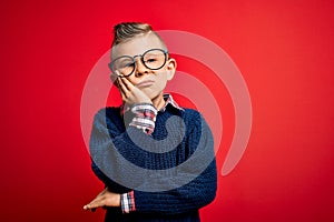 Young little caucasian kid with blue eyes standing wearing smart glasses over red background thinking looking tired and bored with