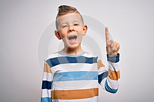 Young little caucasian kid with blue eyes standing wearing striped shirt over isolated background pointing finger up with