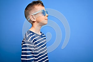 Young little caucasian kid with blue eyes standing wearing sunglasses over blue background looking to side, relax profile pose
