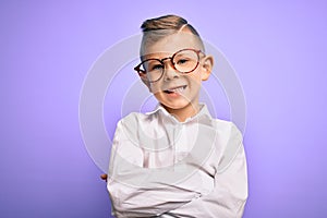 Young little caucasian kid with blue eyes wearing glasses and white shirt over purple background happy face smiling with crossed