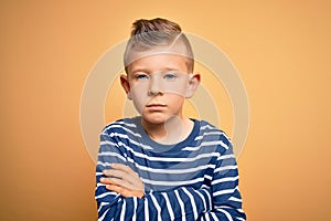 Young little caucasian kid with blue eyes wearing nautical striped shirt over yellow background skeptic and nervous, disapproving