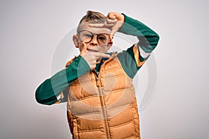 Young little caucasian kid with blue eyes wearing winter coat and smart glasses smiling making frame with hands and fingers with