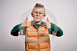 Young little caucasian kid with blue eyes wearing winter coat and smart glasses success sign doing positive gesture with hand,
