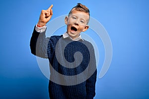 Young little caucasian kid with blue eyes wearing winter sweater over blue background pointing finger up with successful idea