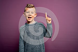 Young little caucasian kid with blue eyes wearing winter sweater standing over purple background pointing finger up with