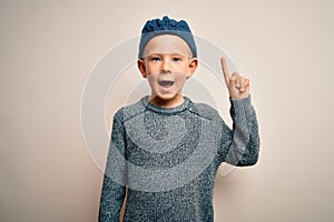 Young little caucasian kid with blue eyes wearing wool cap over isolated background pointing finger up with successful idea