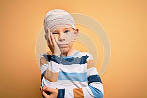 Young little caucasian kid injured wearing medical bandage on head over yellow background thinking looking tired and bored with