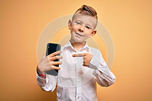 Young little caucasian kid using smartphone and looking at the screen of the phone very happy pointing with hand and finger