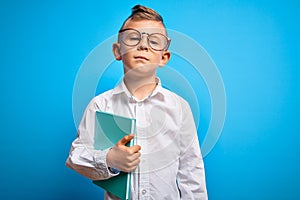 Young little caucasian student kid wearing smart glasses and holding a book from school with a confident expression on smart face