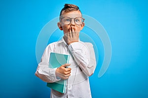 Young little caucasian student kid wearing smart glasses and holding a book from school cover mouth with hand shocked with shame