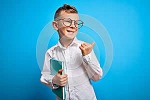 Young little caucasian student kid wearing smart glasses and holding a book from school pointing and showing with thumb up to the